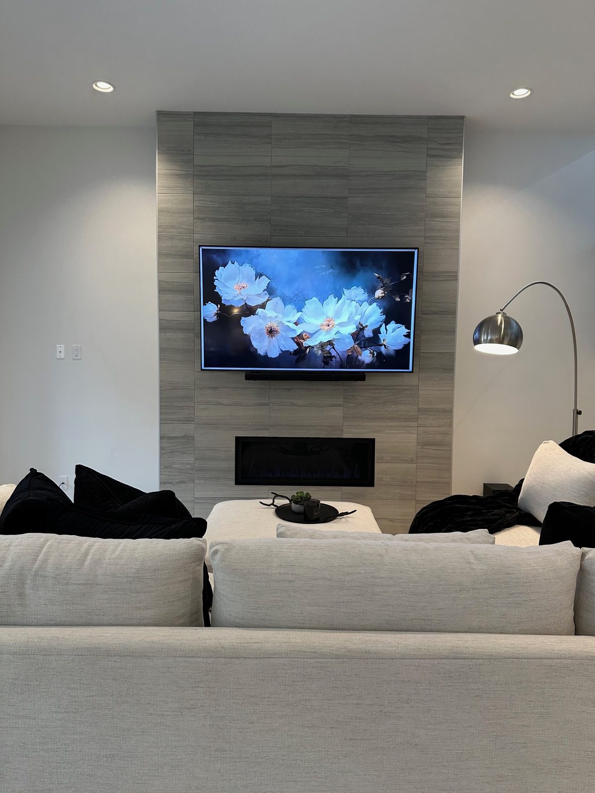 TV and soundbar on a grey porcelain tile chimney above a lit linear fireplace