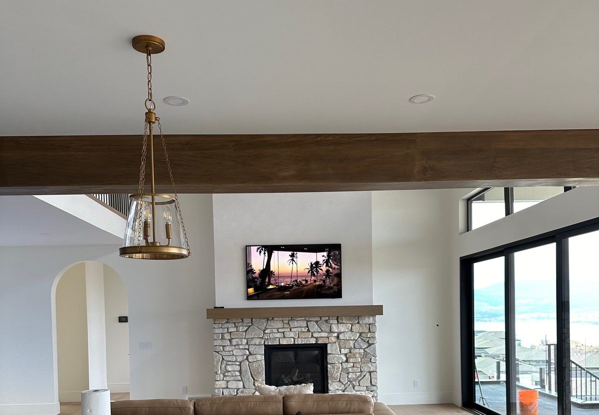 TV mounted above a stone fireplace with a timber mantel in a lake view great room