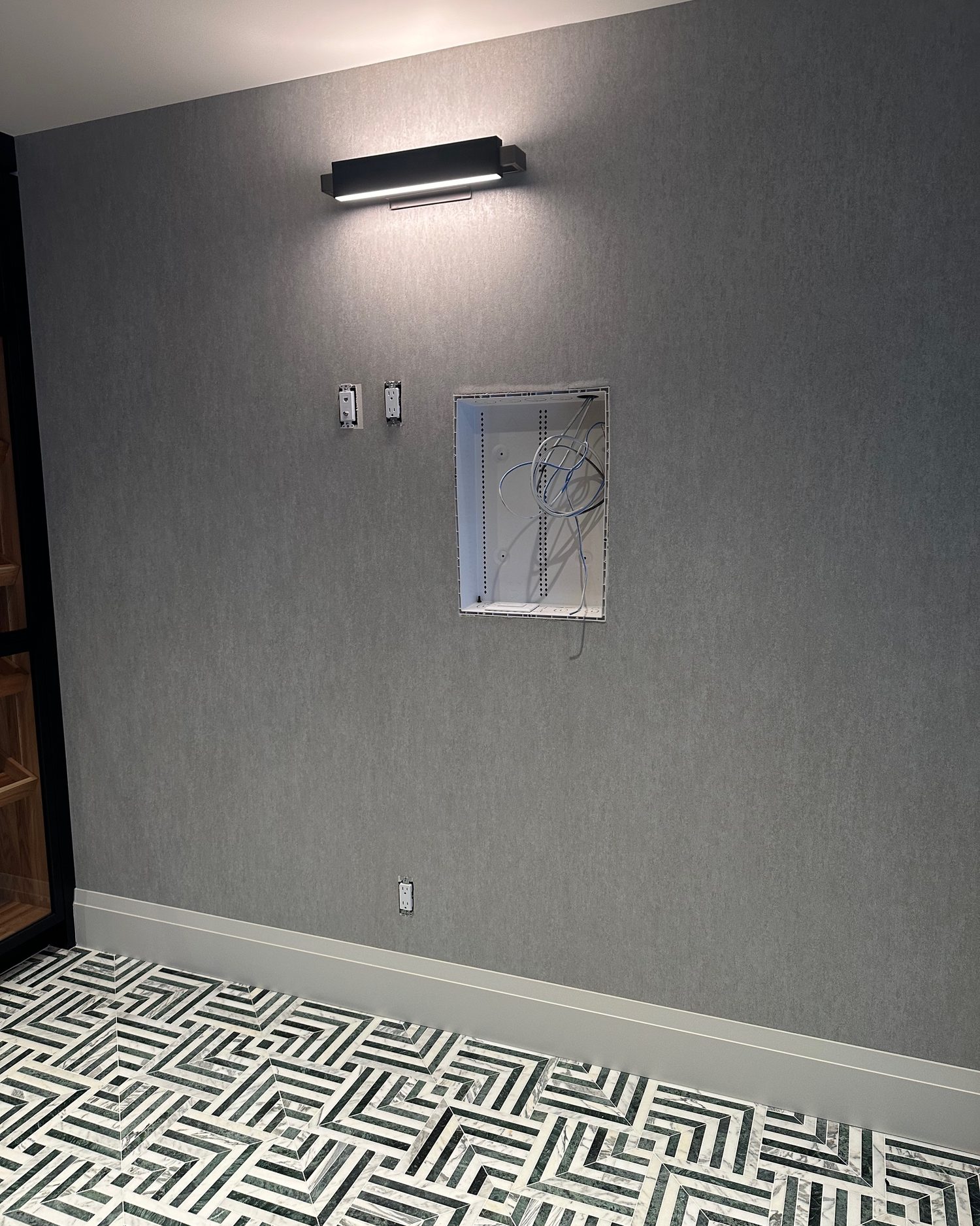 Recessed media box open on the lounge wall with network cable and plates hanging out